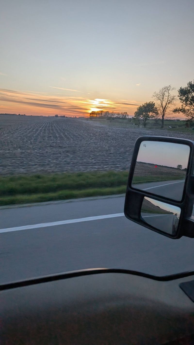 Sunrise over flat farm fields seen through a truck windshield.